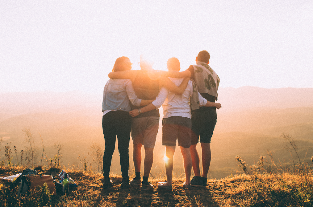 Stock photo of a group of four young adults outdoors on a cliff overlooking mountains at sunset